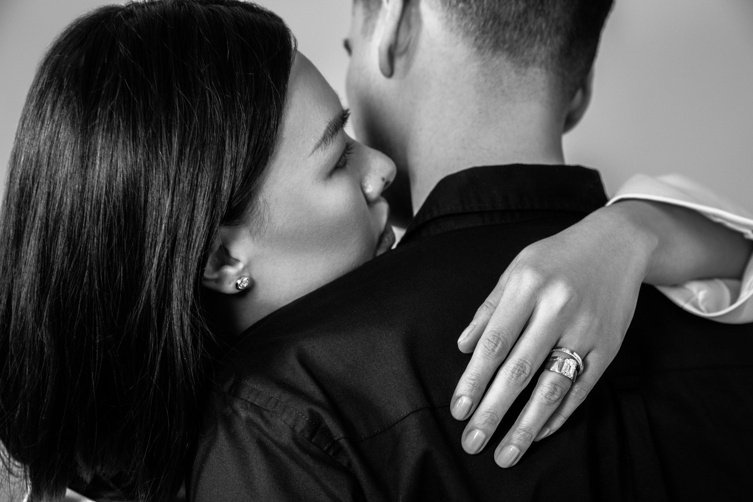 a model wearing the venus pendant and two custom engagement rings, in black and white with their arm wrapped around their husband. Learn more about sophie ratner custom bridal designs.