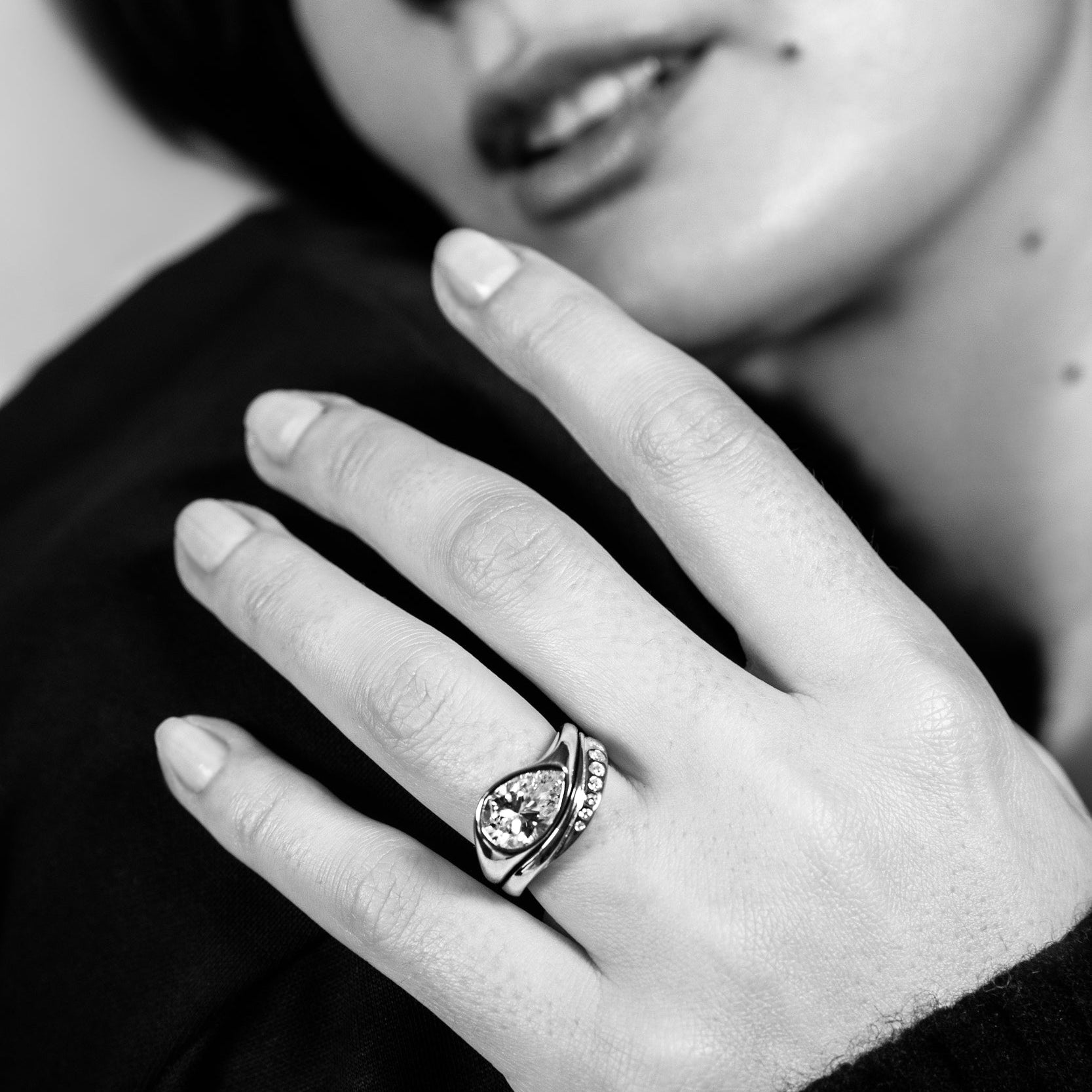 a women resting her hand on her boyfriend in a black and white image modeling a custom diamond engagement ring and wedding band designed by Sophie Ratner. Learn moer about custom designs