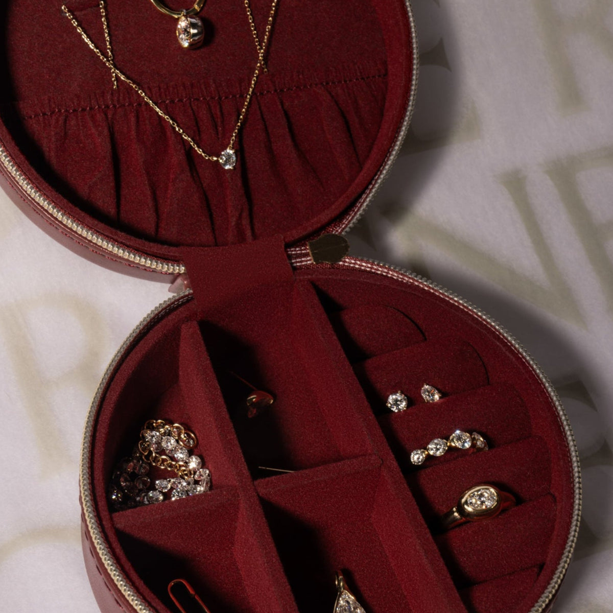 A round Free Special Edition Jewelry Case lined in deep red velvet, containing a gold necklace, several rings, and stud earrings.