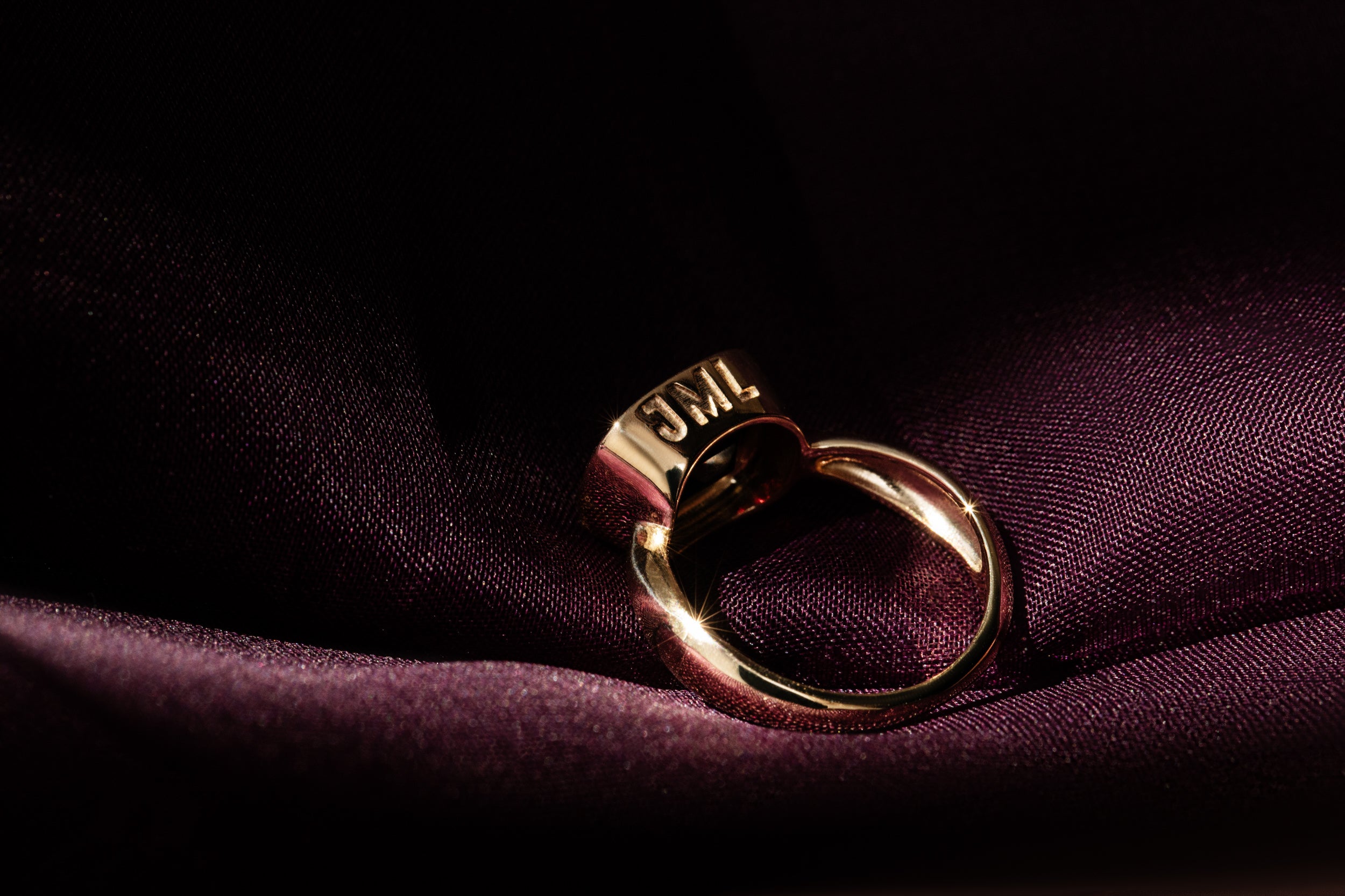 A Sophie Ratner gold and garnet Custom Ring sits on a purple sating fabric. The ring is engraved with initials, promoting our pieces to personalize collection. Shop engravable and cusotmizable gifts.