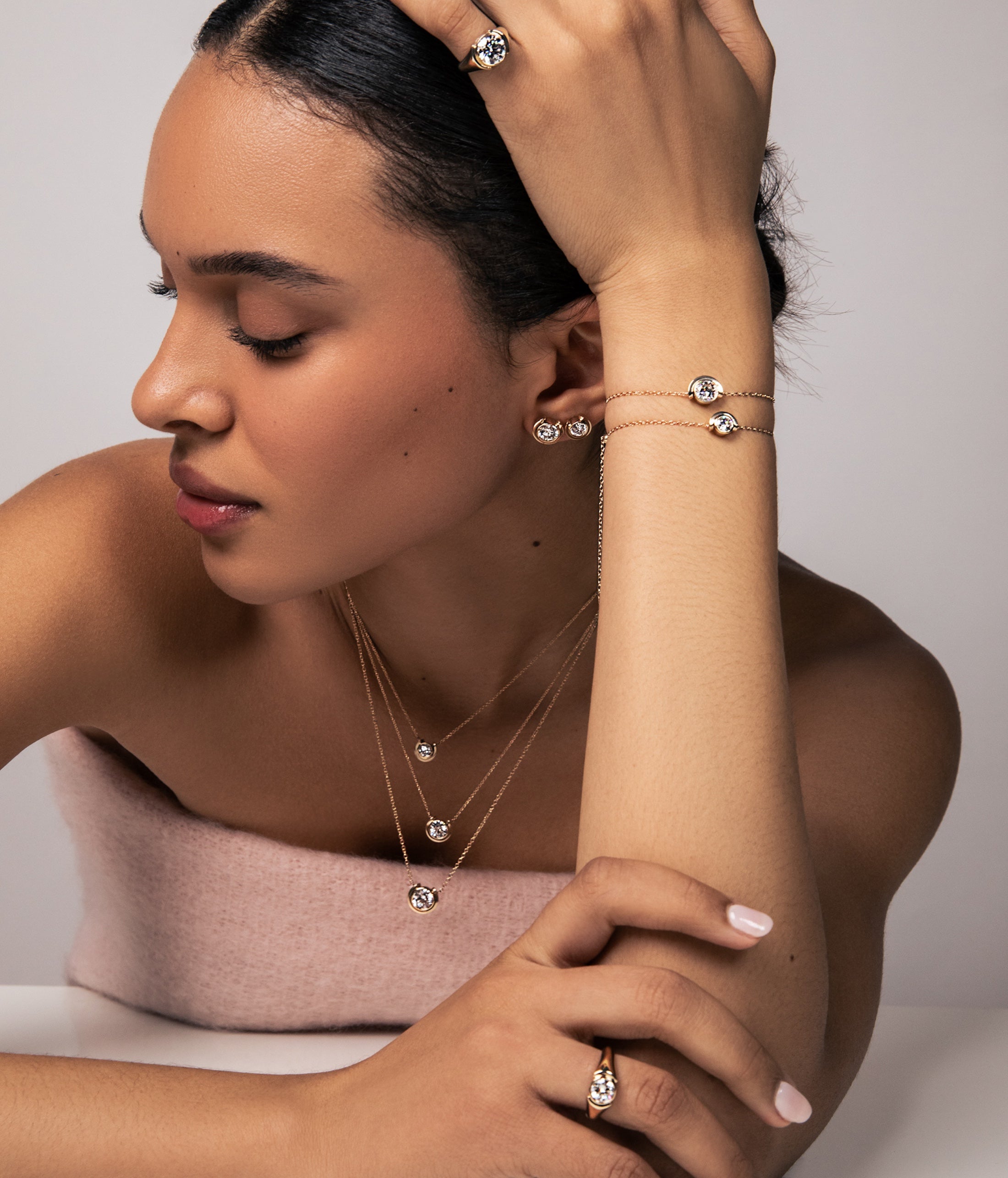 Woman wearing multiple pieces of fine jewelry from sophie ratner's latest timekeepr collection. including necklaces, bracelets, and rings on a neutral background. shop her latest designs.