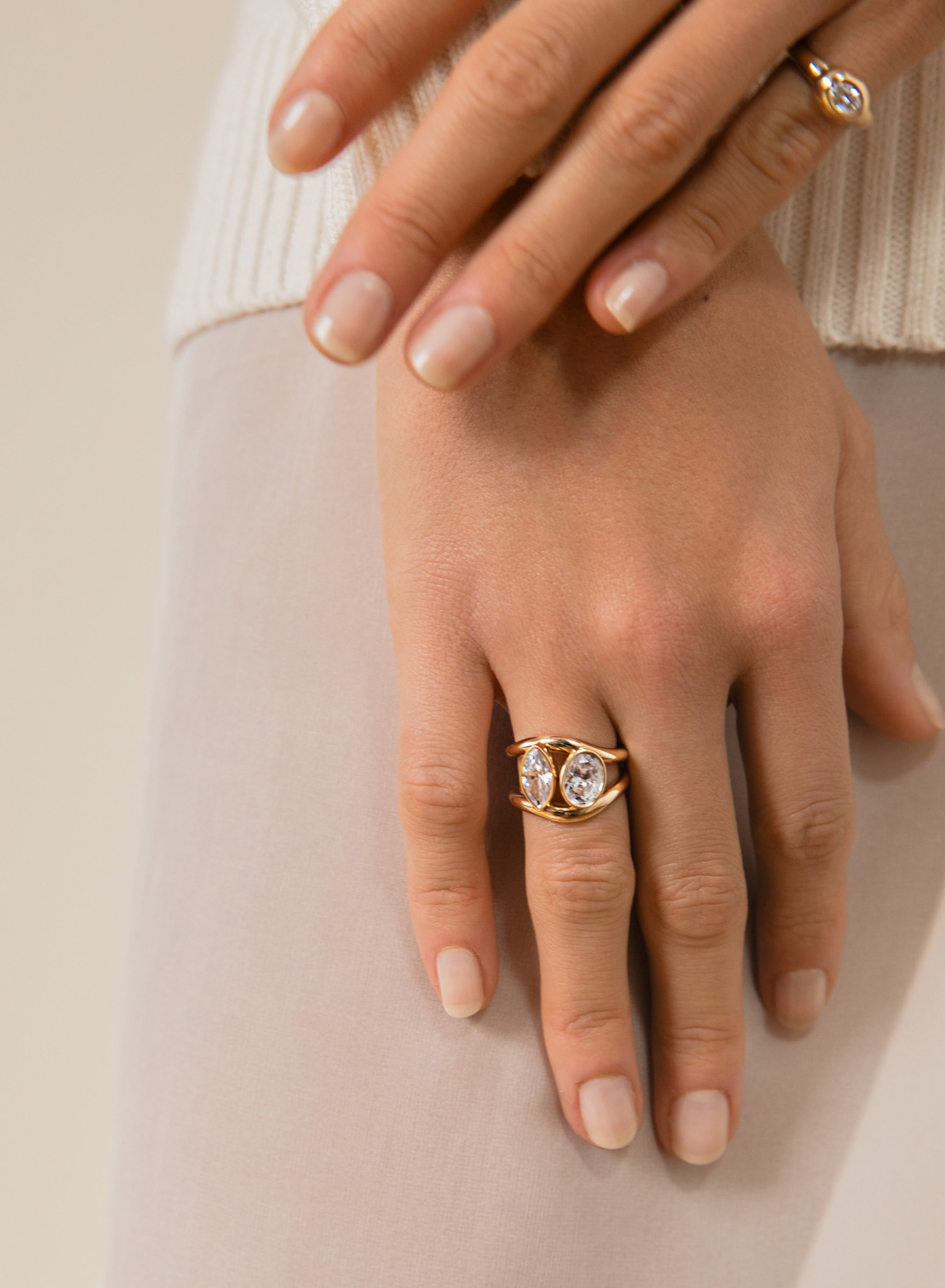 Hand wearing a gold ring with a diamond on a neutral background