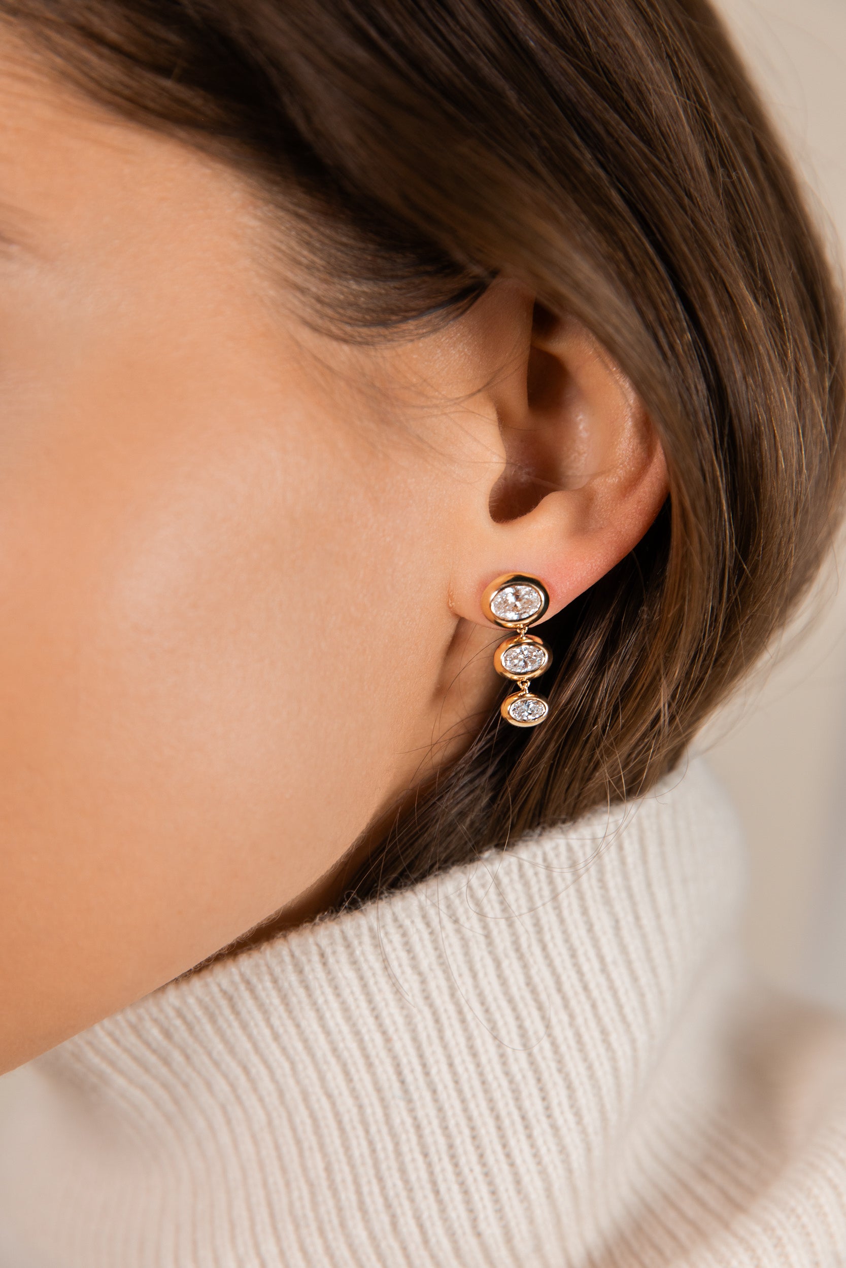 Close-up of a model wearing the lab grown oval diamond and solid 14k gold venus triple drop earrings.