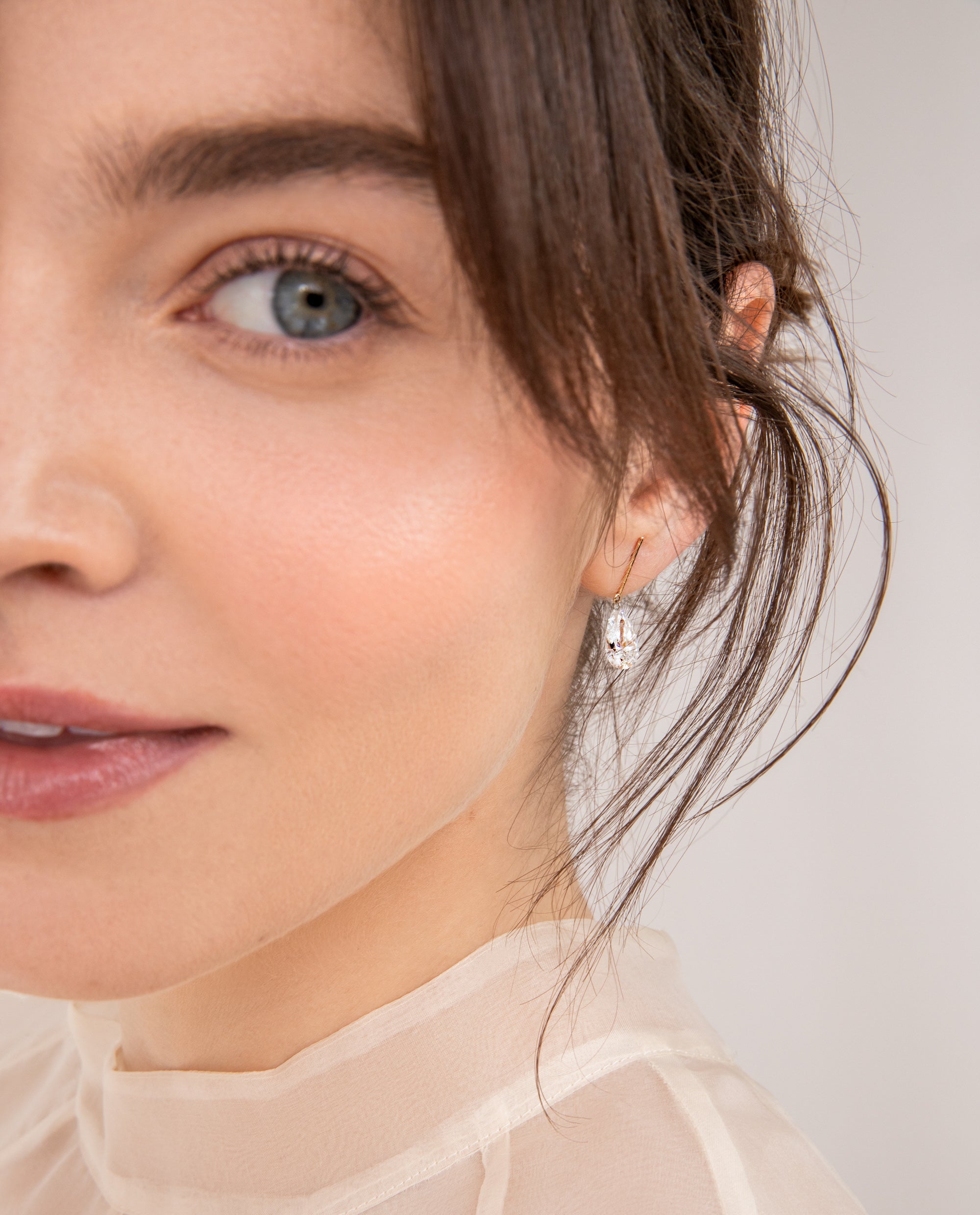 a fair model wears the new 2 carat pear and gold bar earrings made for sophie ratner bridal. a lab grown pear diamond pierced and dangling on a solid 14k gold bar.