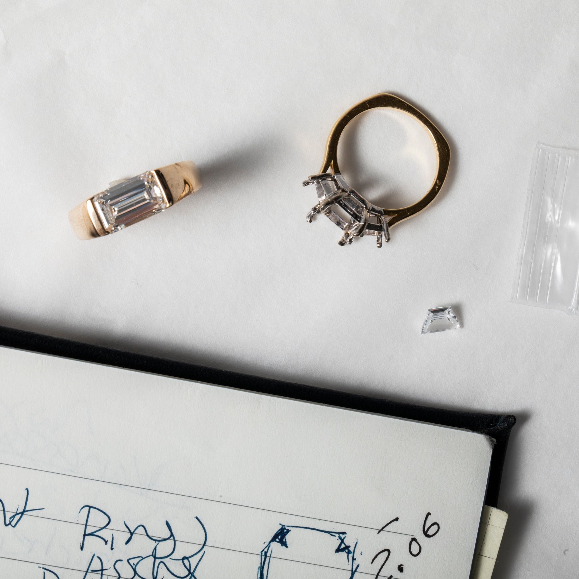 Two diamond rings on a white surface with a notebook and pen.