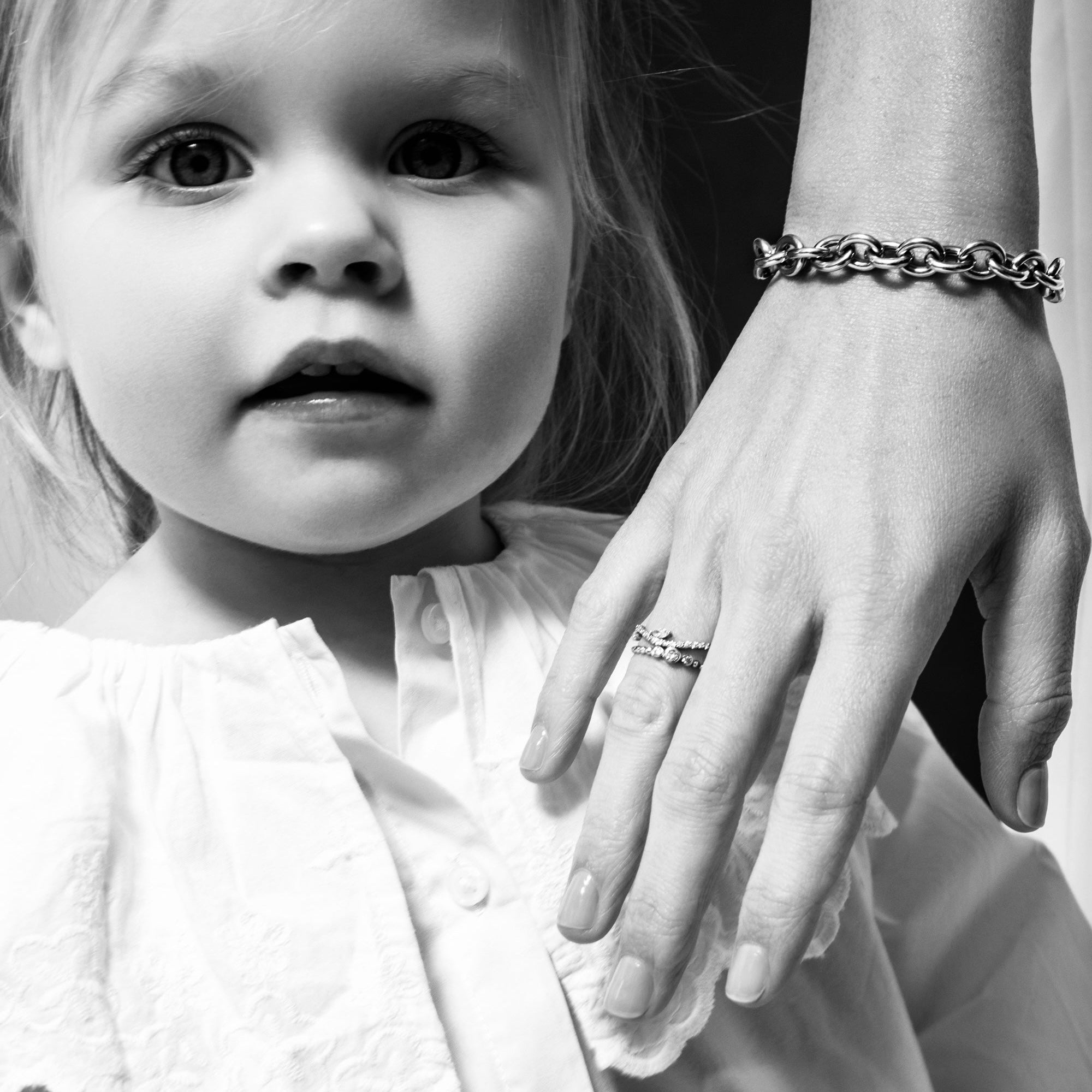 Black and white photo of a child wearing a dress with a lace collar, with an adult's hand resting on the child's shoulder.