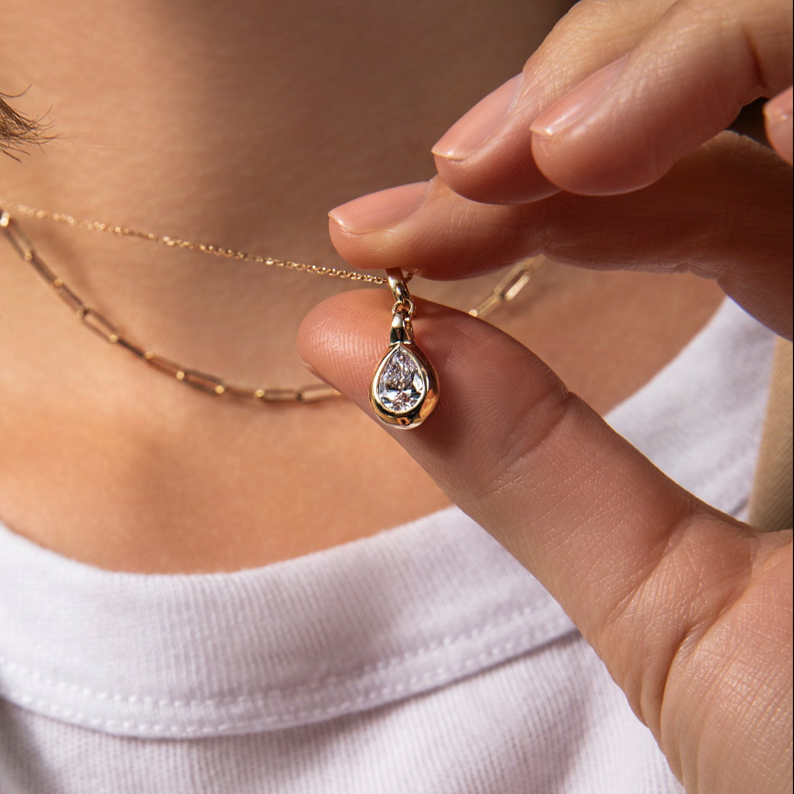 Person holding a gold necklace with a teardrop pendant
