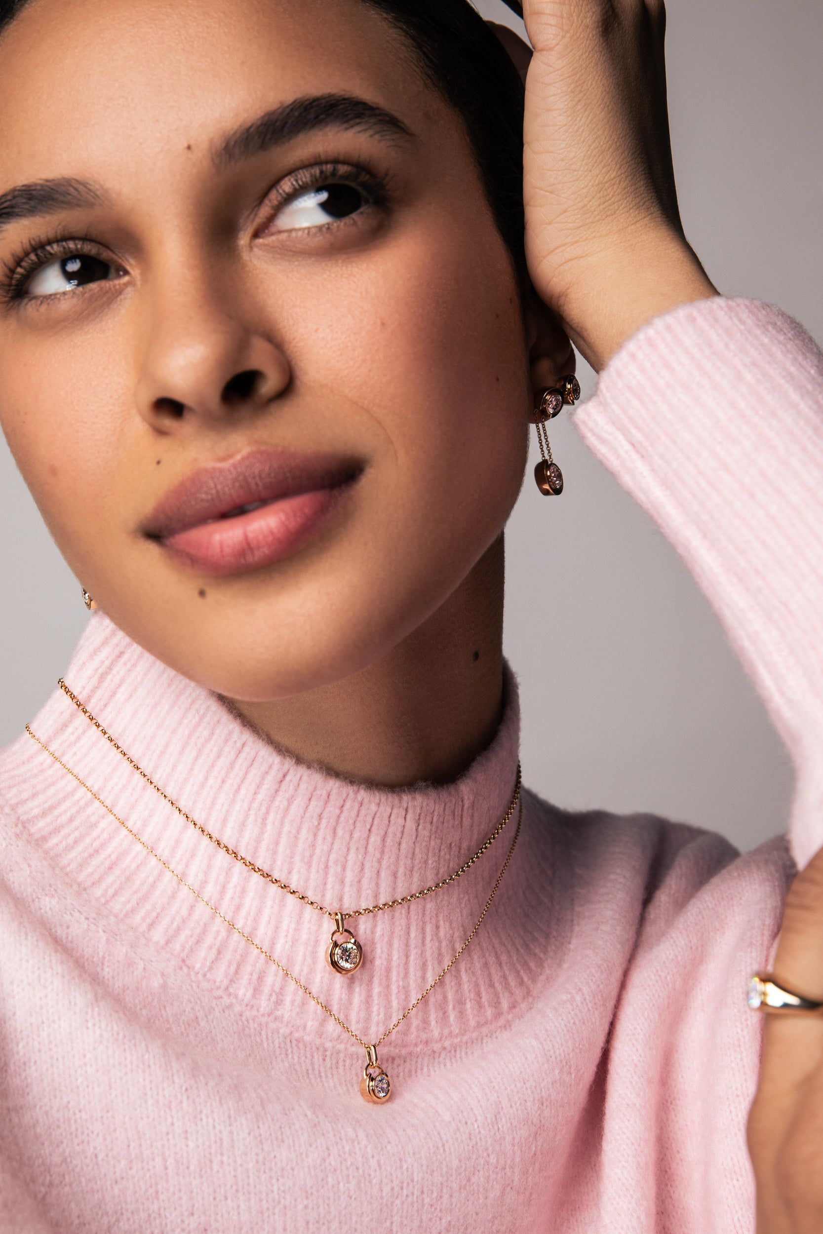 Woman wearing a pink sweater and gold jewelry with a neutral background