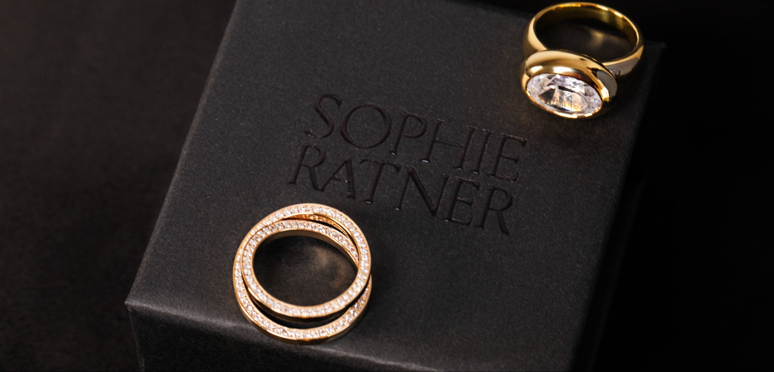 Two solid 18k gold and lab grown diamond custom rings designed by sophie ratner place on top of a branded ring box. showcasing custom bridal and engagement designs. learn more about the custom design process.