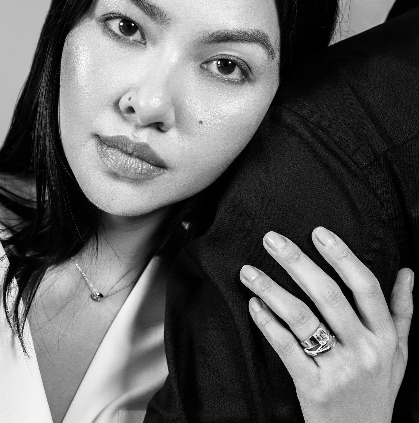 a model wearing the venus pendant and two custom engagement rings, in black and white with their arm wrapped around their husband. Learn more about sophie ratner custom bridal designs. 