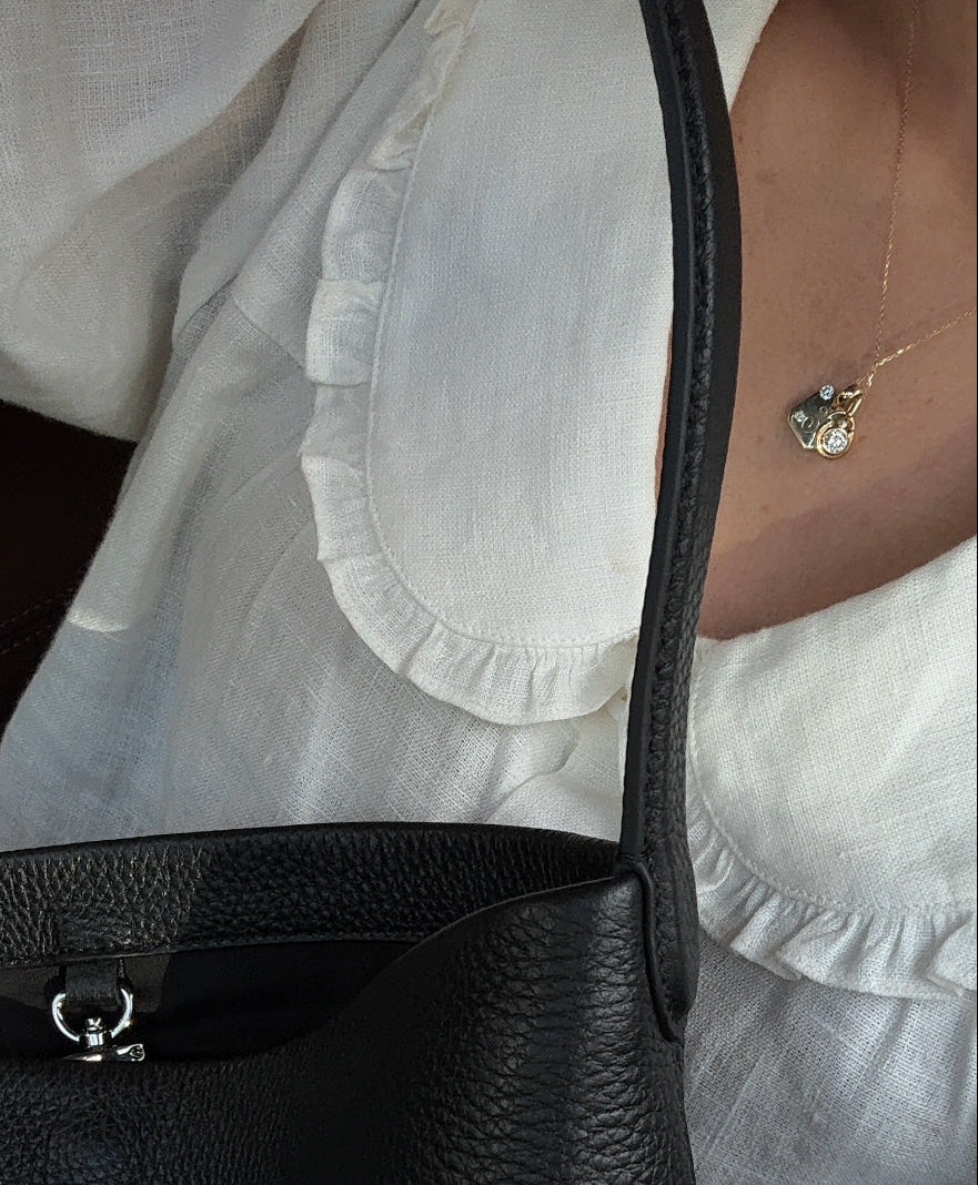 Black handbag held by a person wearing a white shirt.