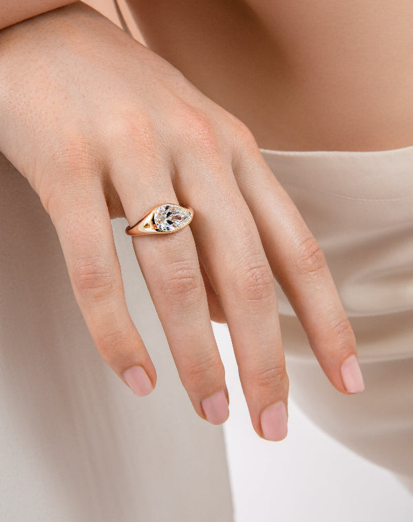 Hand wearing a rose gold ring with a clear gemstone on a neutral background