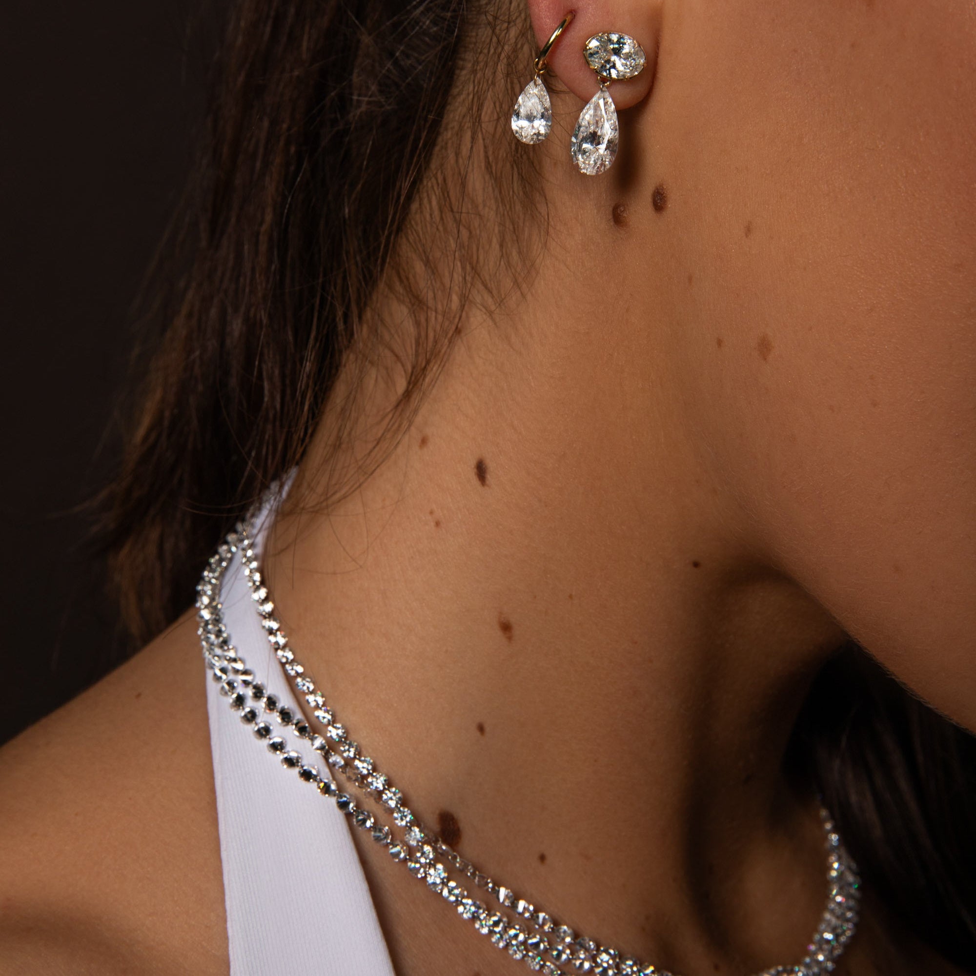 Close-up of a person wearing a silver necklace and earrings with a dark background