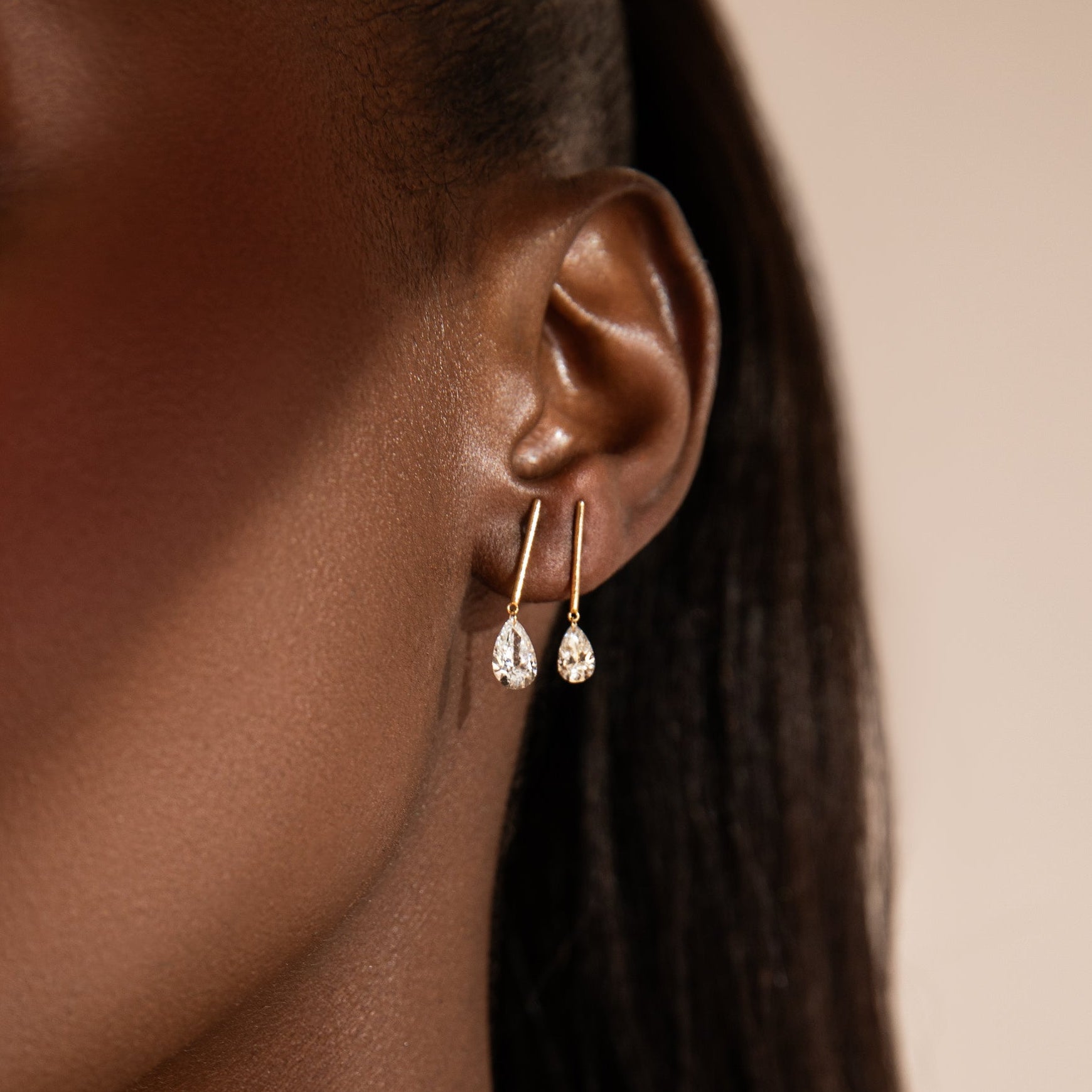 Close-up of a person wearing gold earrings and a delicate gold necklace against a neutral background