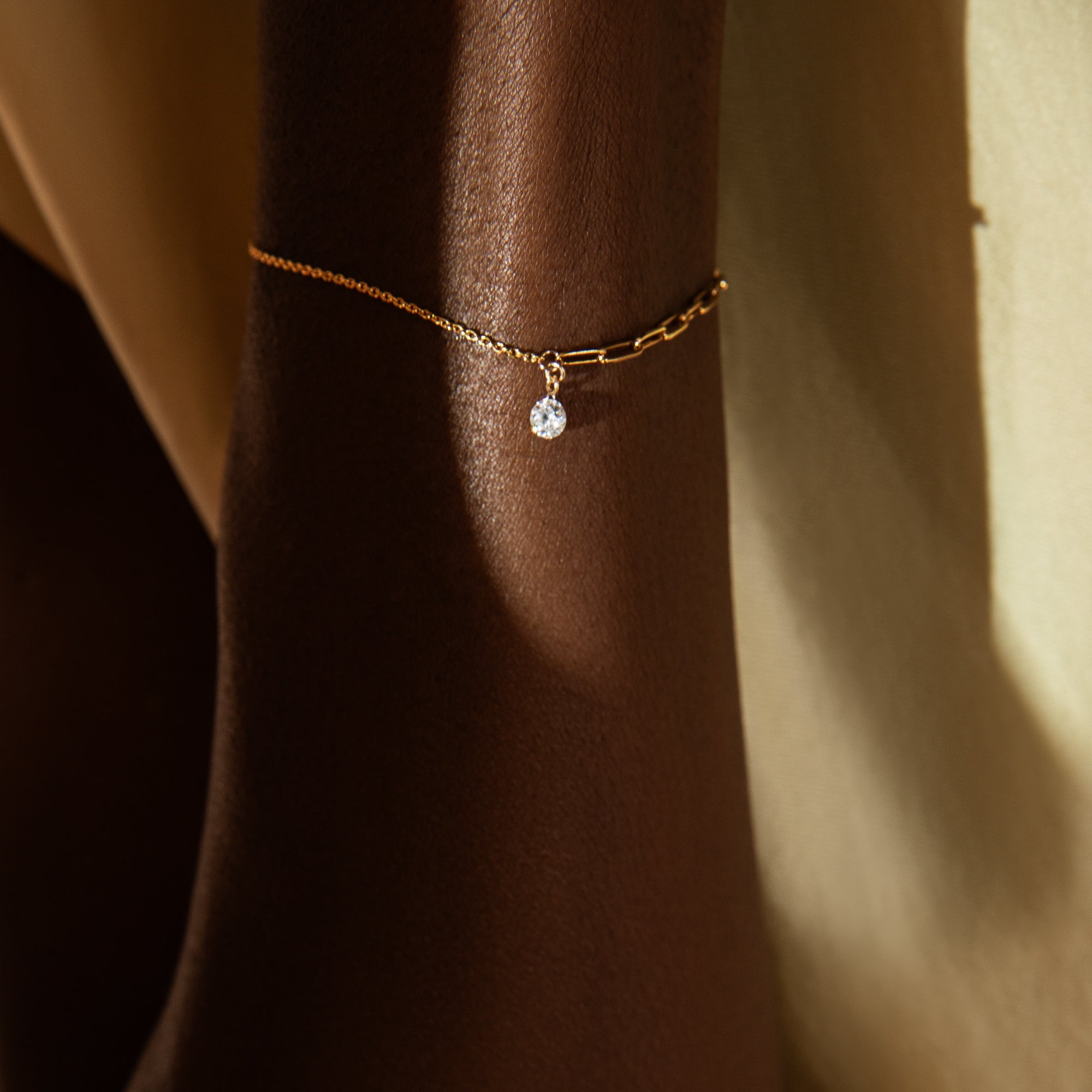 Gold bracelet with a small round gemstone on a wrist against a neutral background