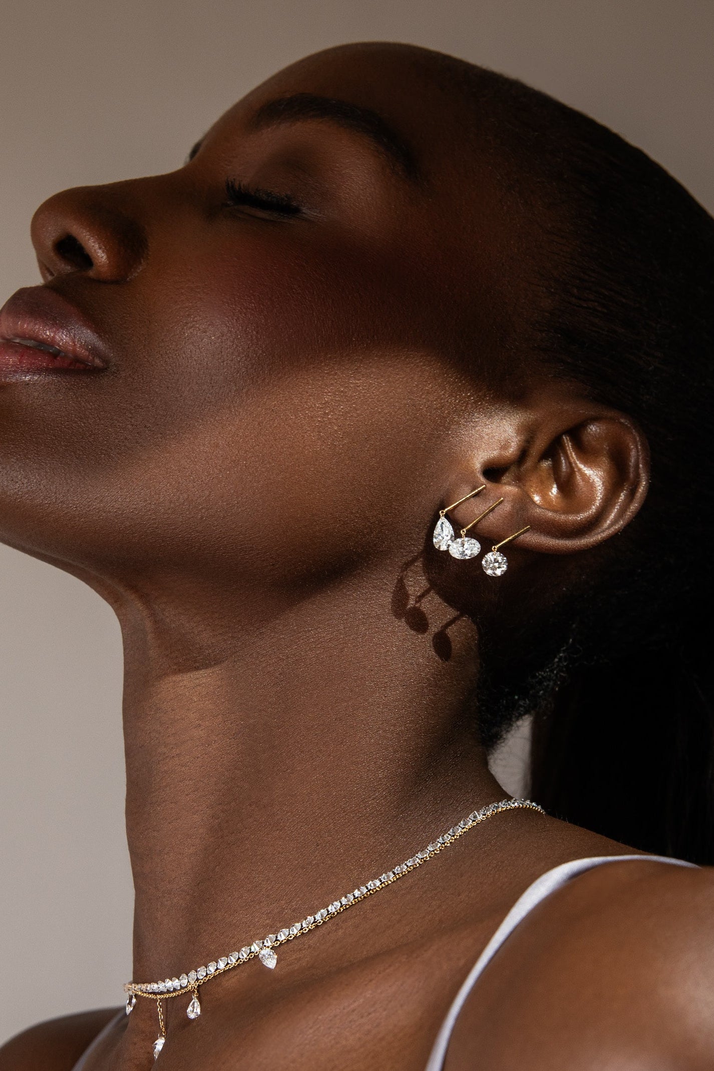 Woman wearing gold earrings and a necklace against a neutral background