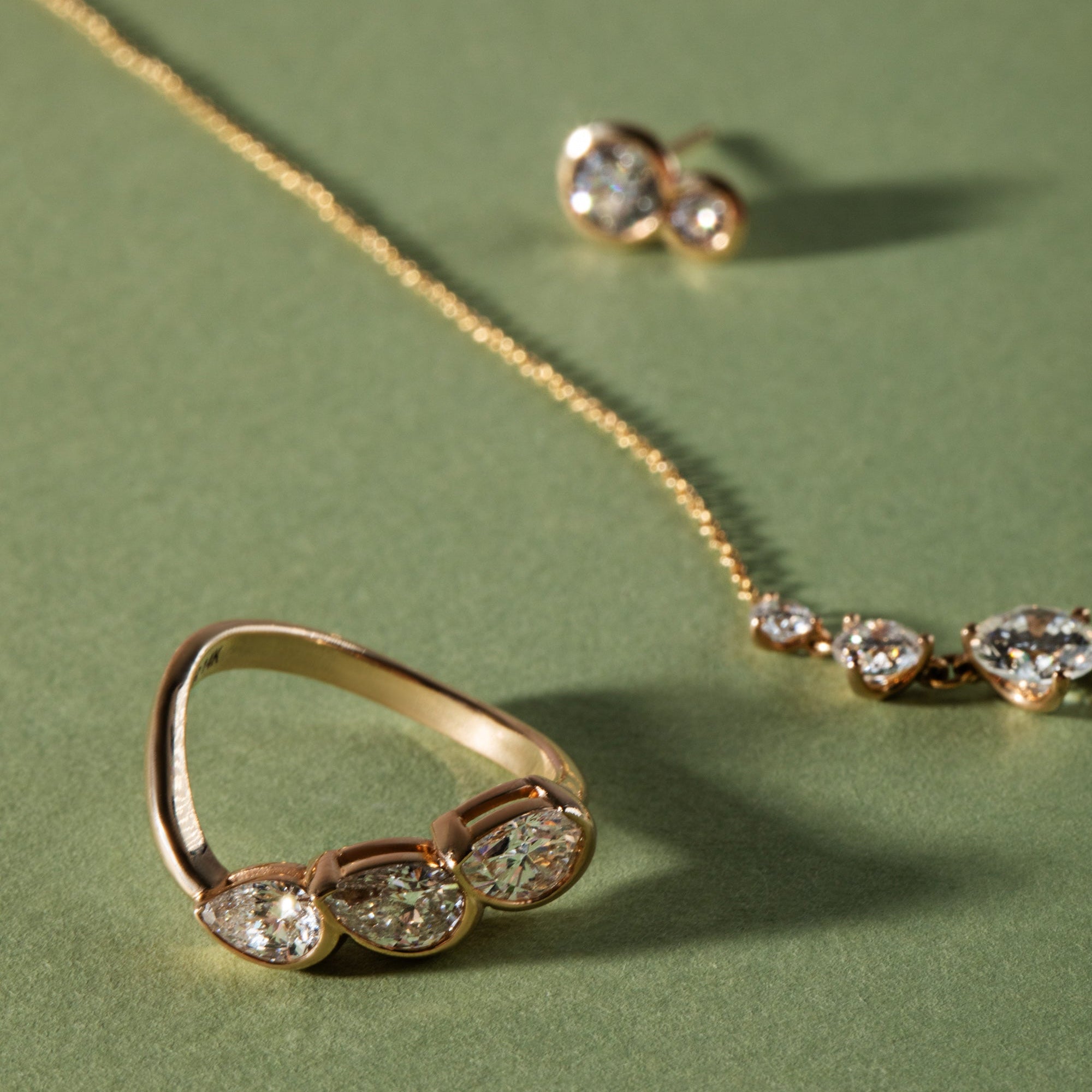Gold jewelry set with ring, earrings, and necklace on a green background