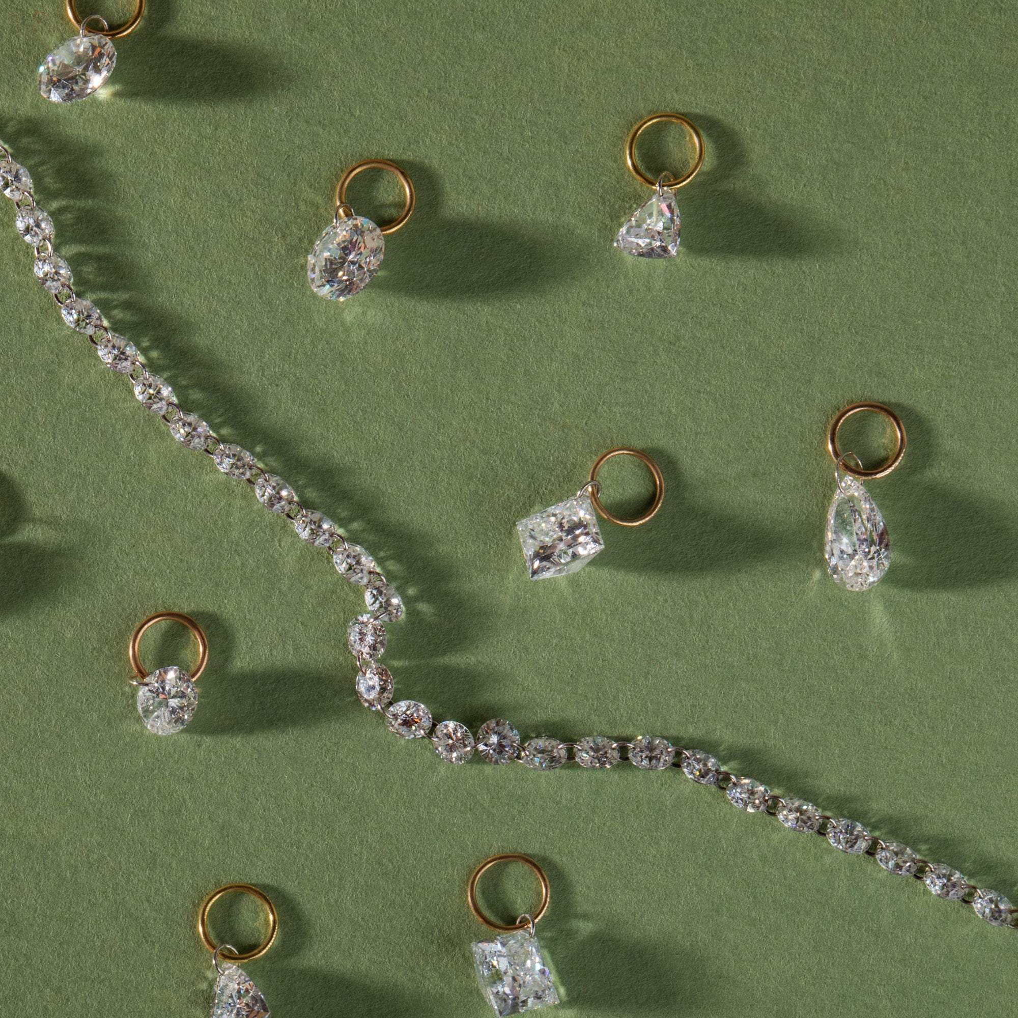 the pierced diamond tennis necklace and earrings charms scattered on a green background
