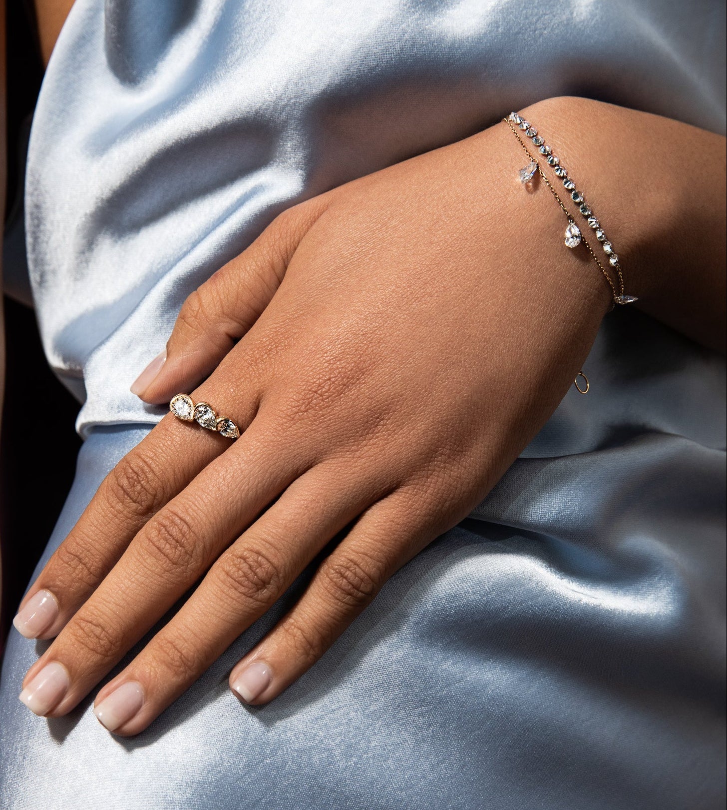 Close-up of a hand wearing a ring and bracelet on a light blue fabric background