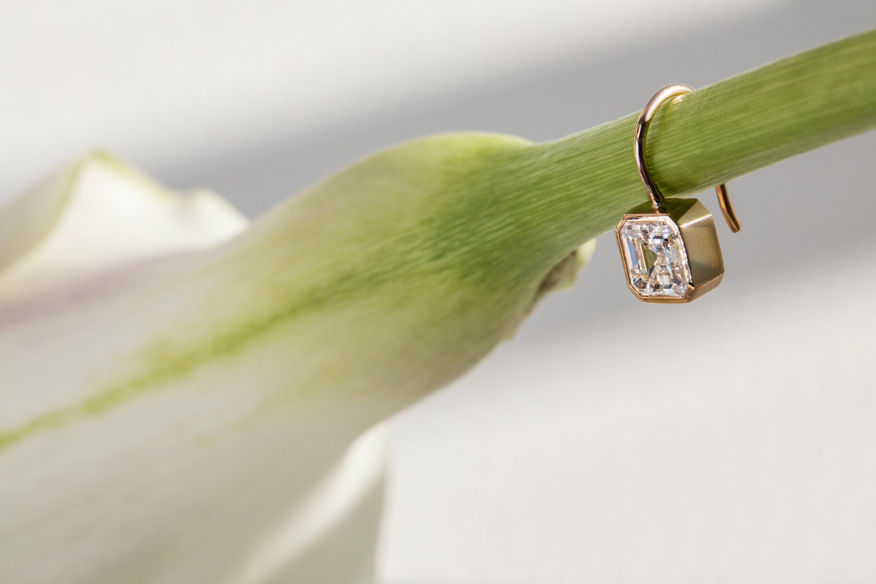A lab grown asscher diamond and 14k gold drop earring hanging on a cala lily stem. shop sophie ratner's latest bridal jewelry designs.