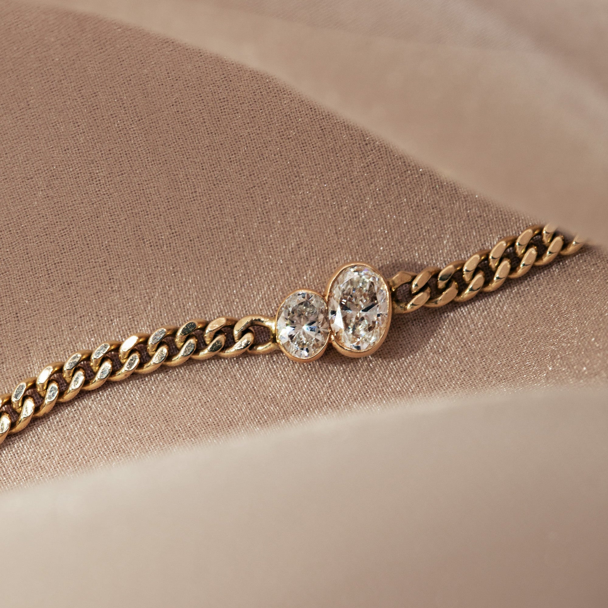 The duet oval bracelet in 14k yellow gold is showcased in a wave of lush blush pink and cream fabric. shop in stock for valentine's day. 