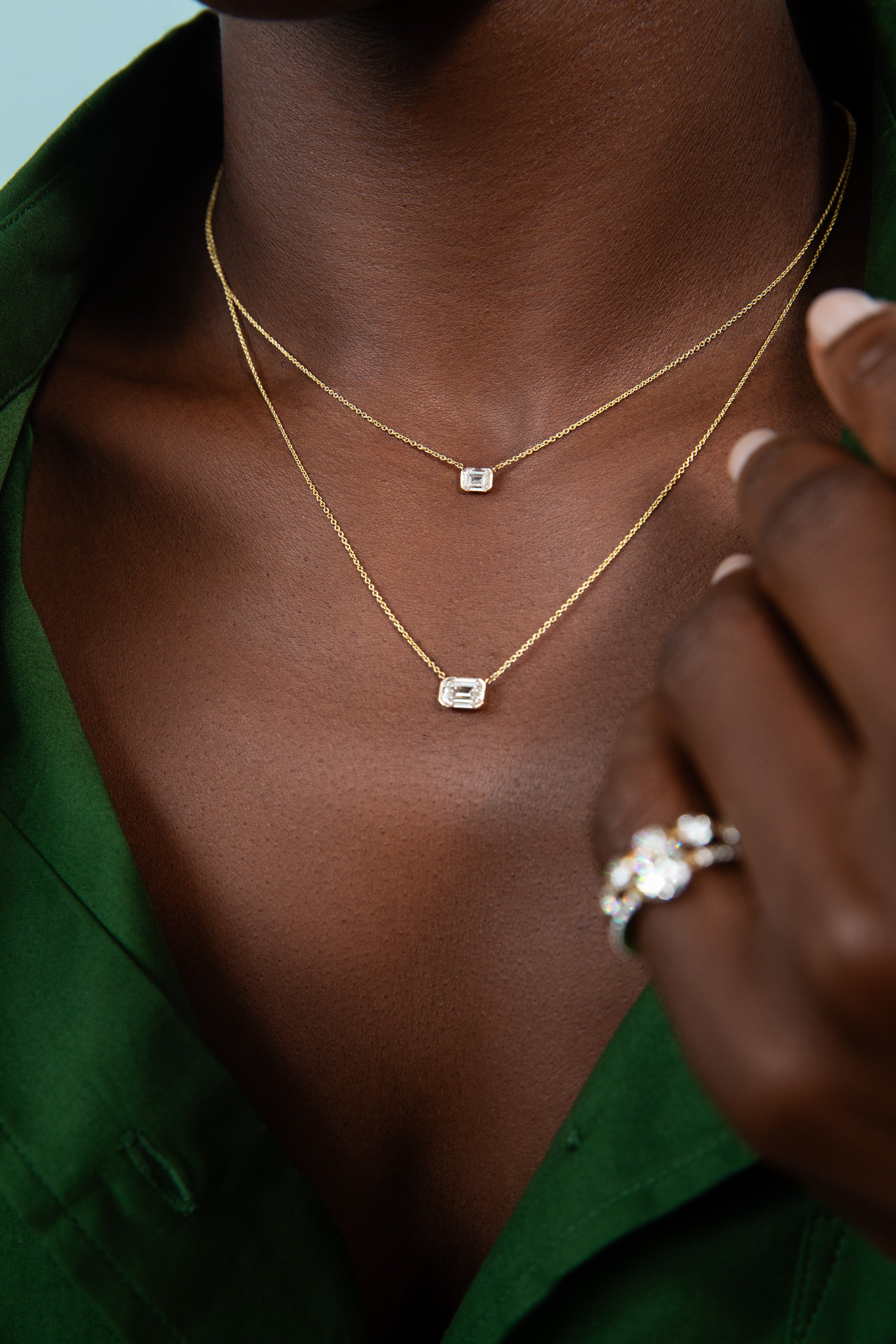 Awa models the large and meidum emerald sunrise pendant.  a lab grown emerald cut diamond in a solid 14k gold v split bezel. shop the new fall collection. 