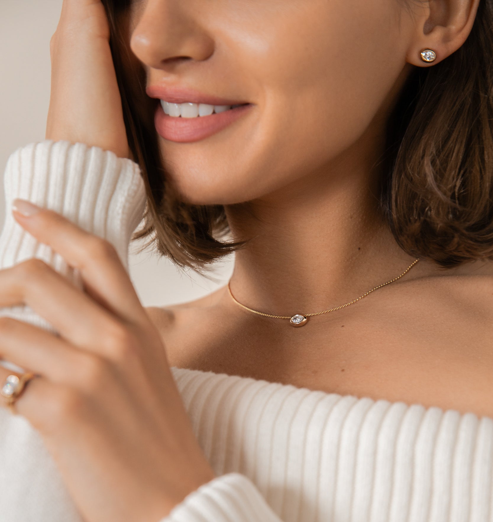 Close-up of a woman wearing a delicate necklace with a pearl pendant, dressed in a white sweater.