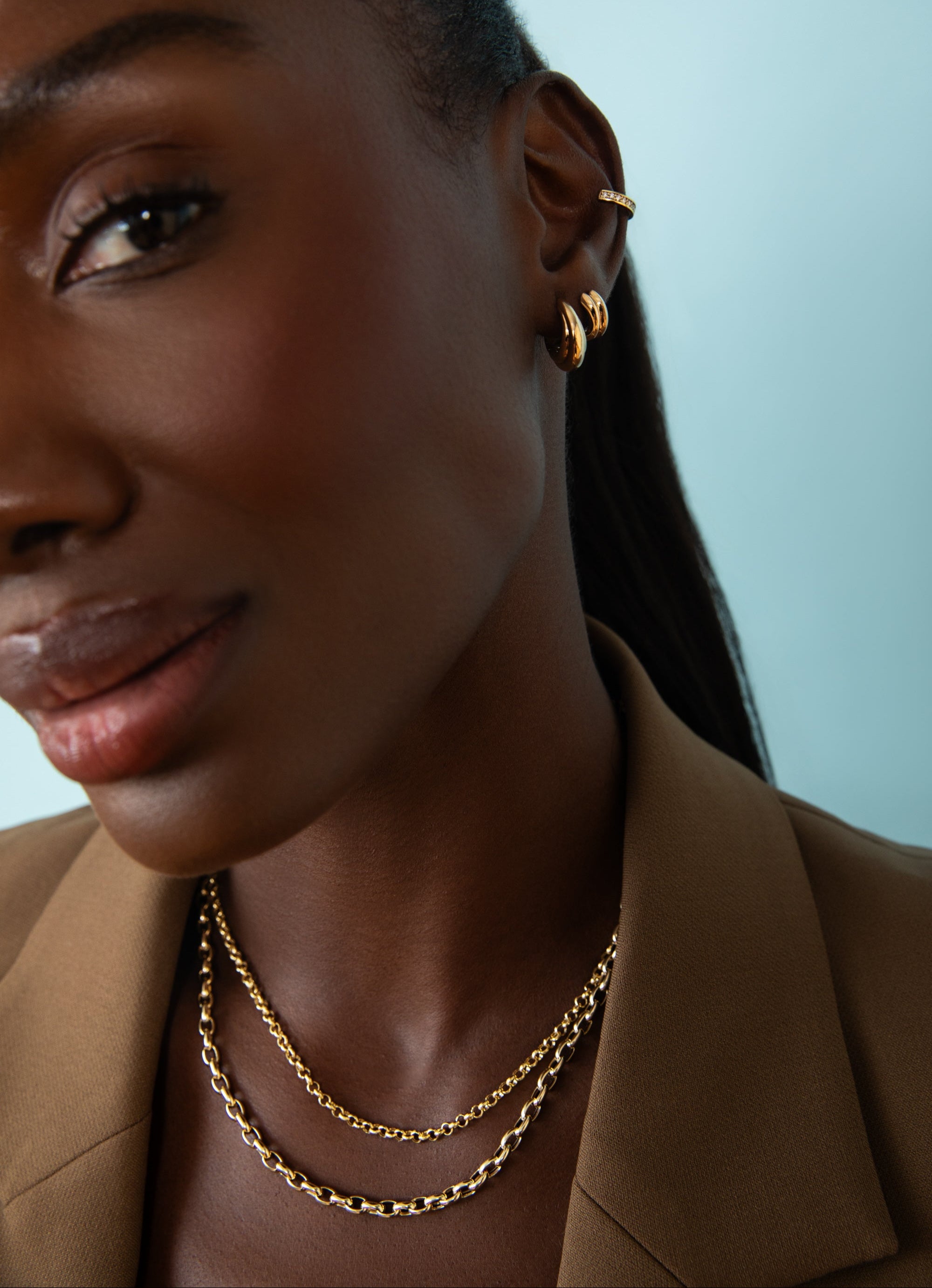A darker skin model wears the new fall collection including solid 14k gold chain, hoops and rings. shop fall favorites. 